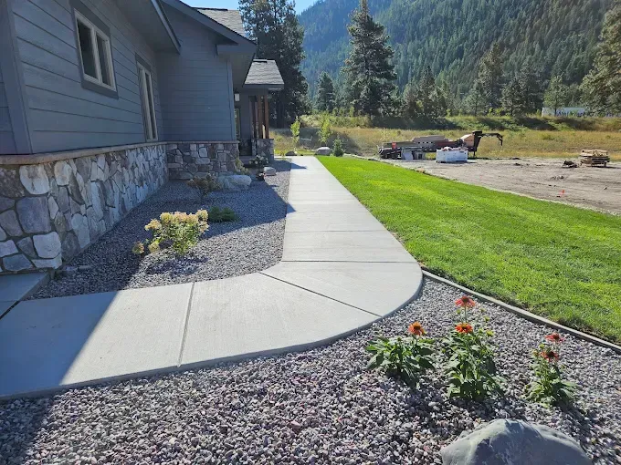 A concrete walkway leading to a house with mountains in the background