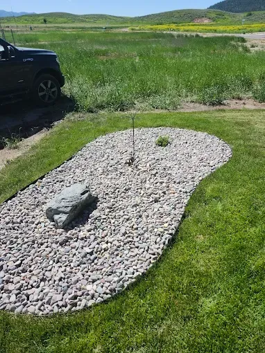 A black truck is parked in a grassy field next to a gravel area.