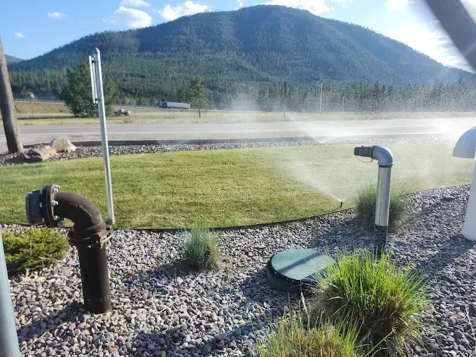 A sprinkler is spraying water on a lush green field with mountains in the background.