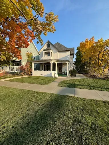 A white house with a large lawn and trees in front of it.