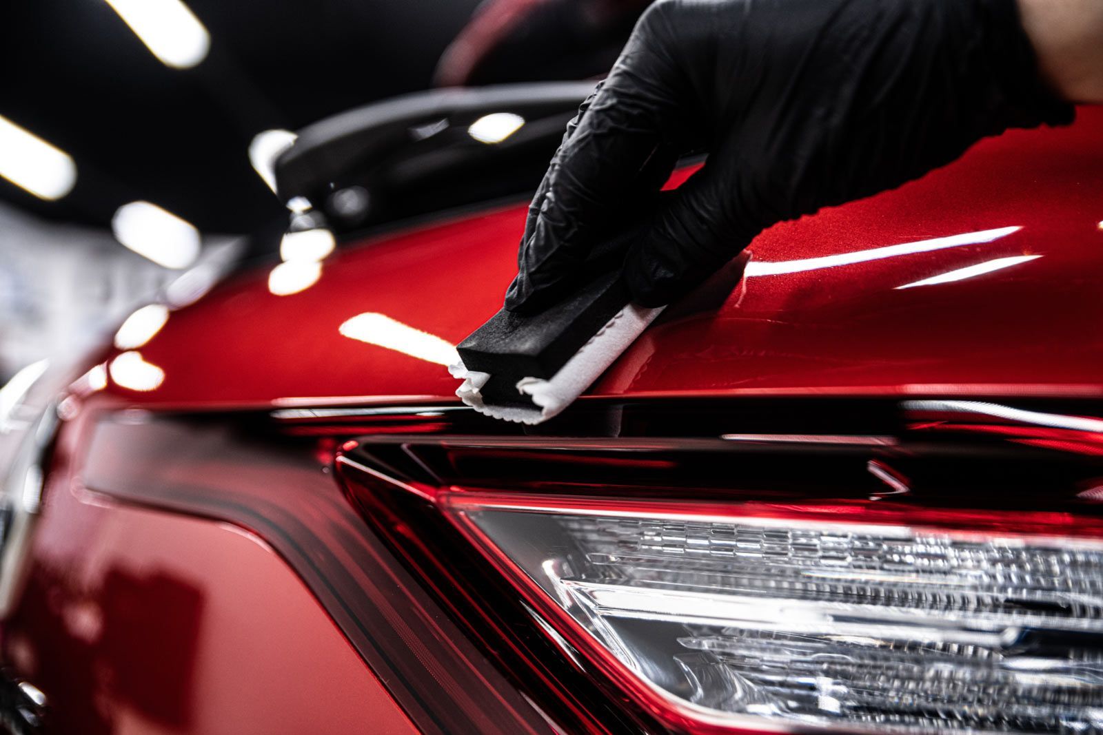Gloved hand applying ceramic coating to a red car's hood, near a headlight.