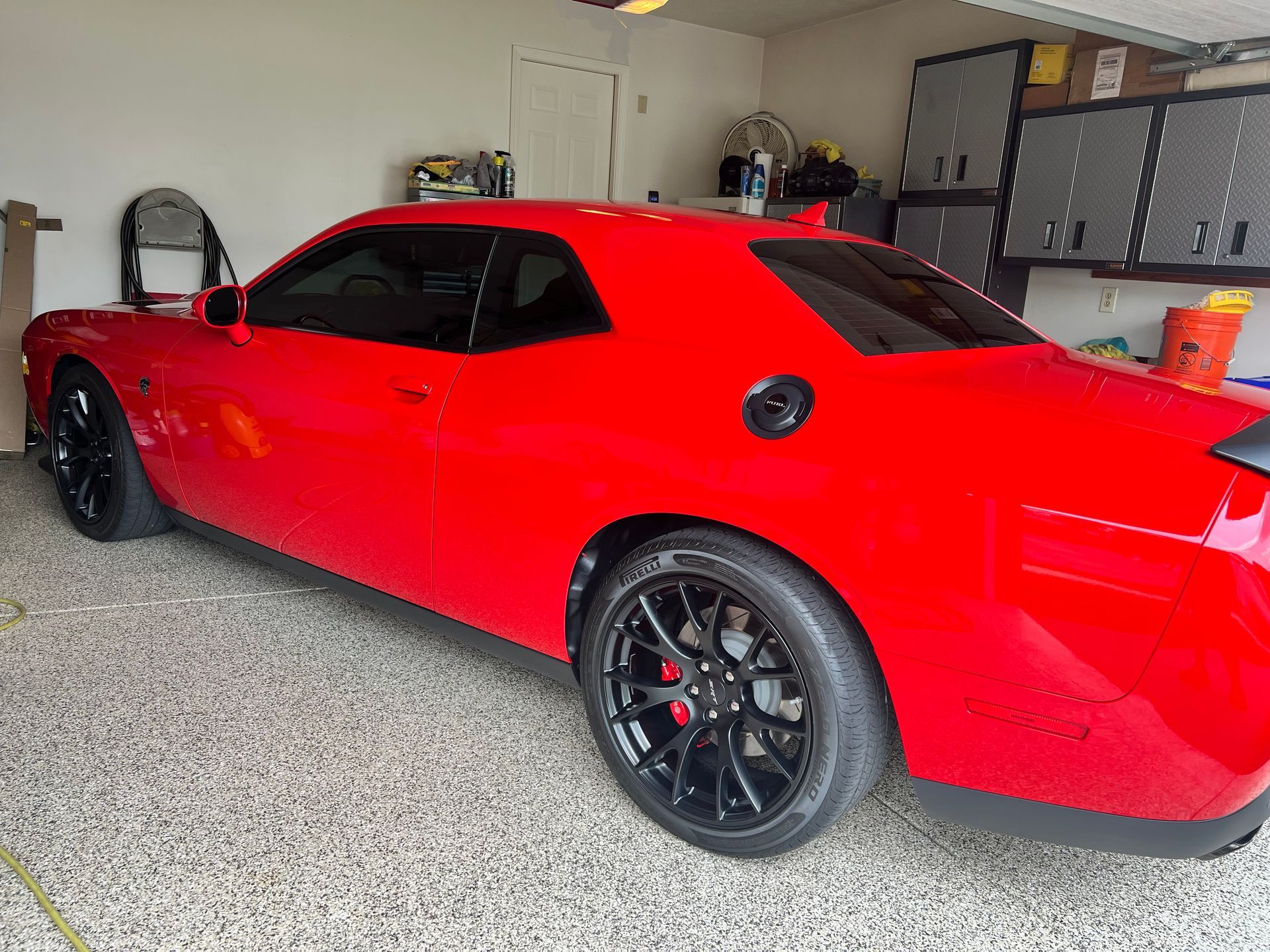 Red Dodge Challenger in a garage with black wheels.