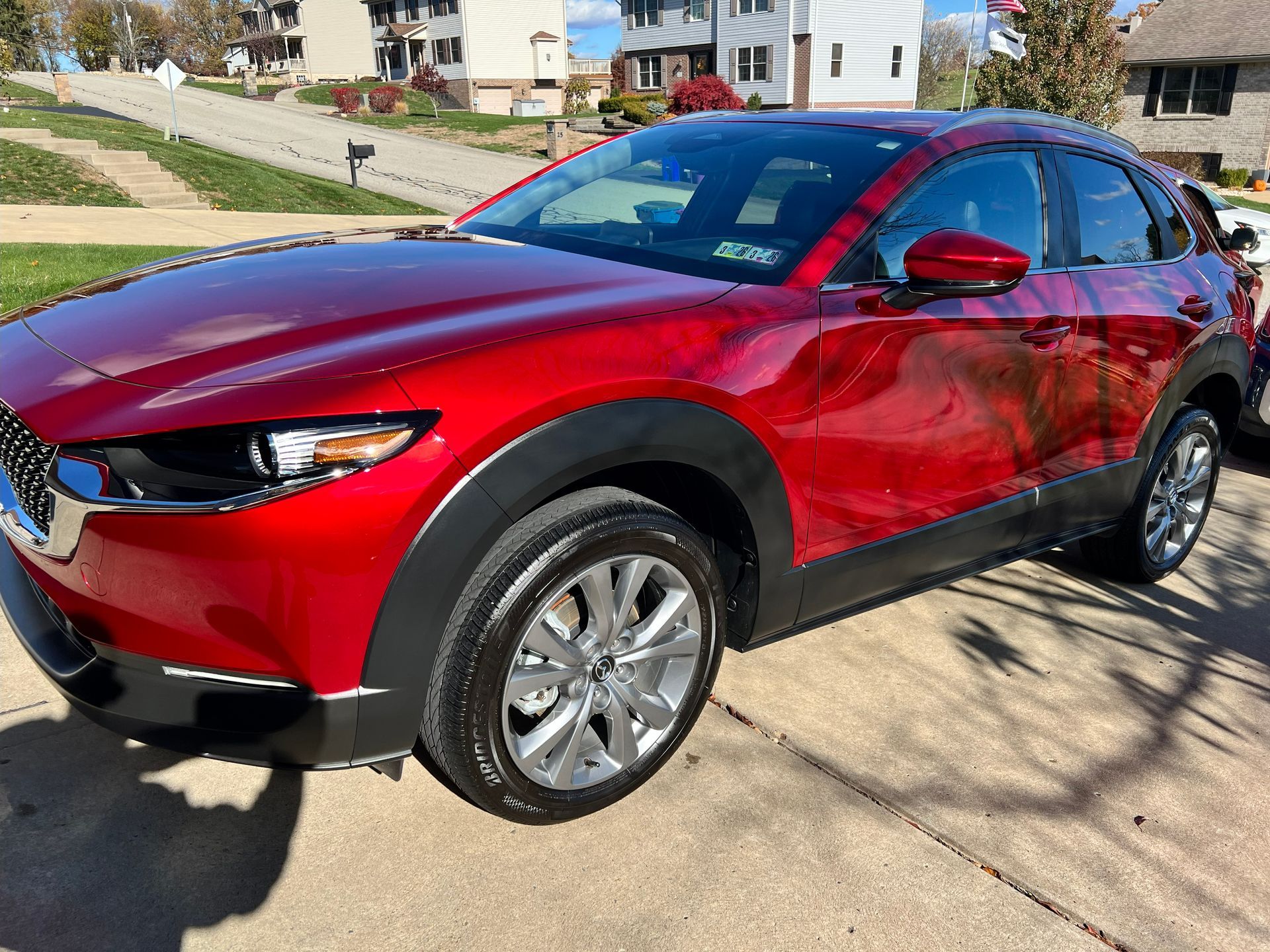Red Mazda CX-30 SUV parked on a paved driveway in front of a residential neighborhood on a sunny day.