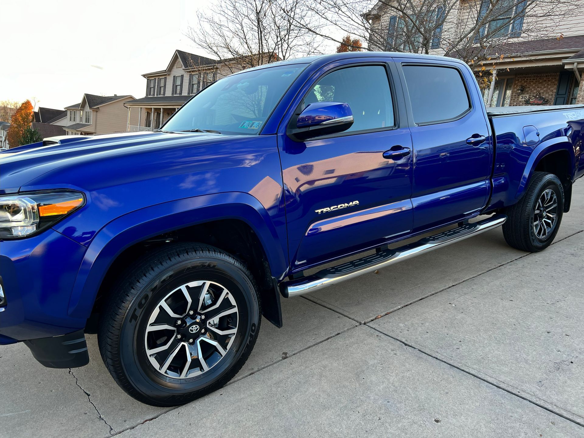 Blue Toyota Tacoma truck parked on a driveway in front of houses.