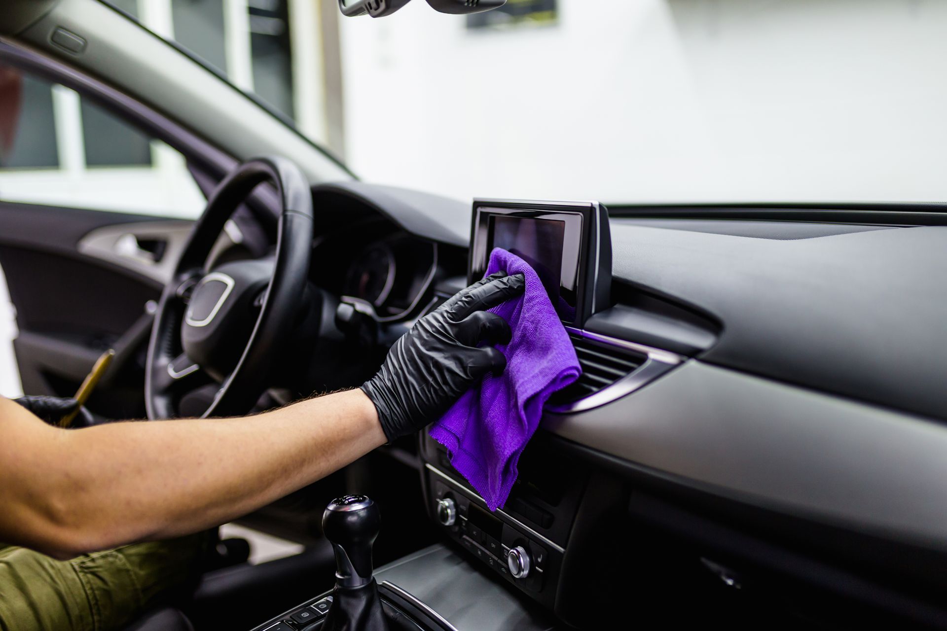 Person wearing black gloves cleaning a car dashboard with a purple cloth.
