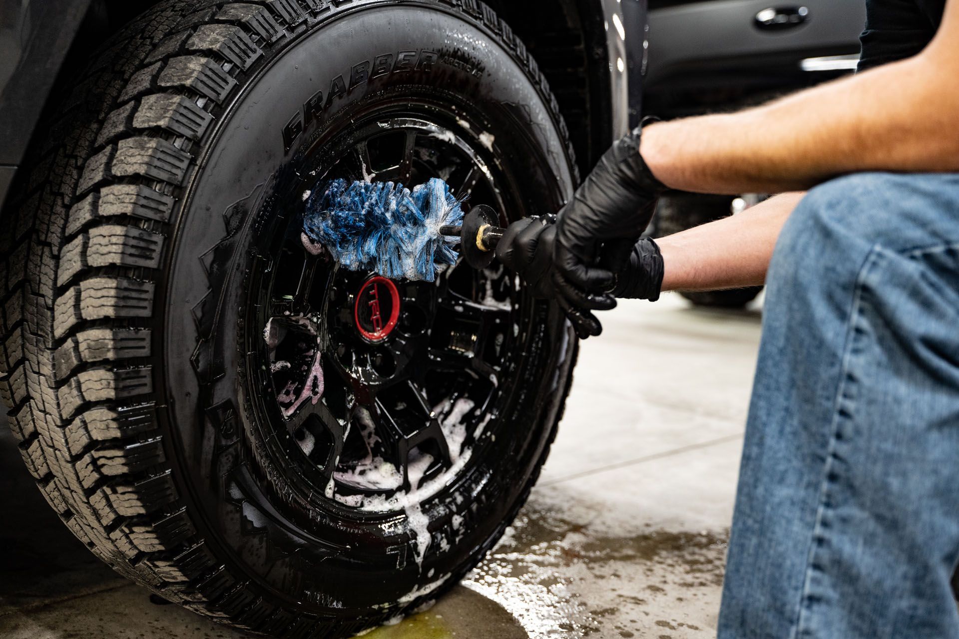 Person washing a black car tire with a brush and soapy water.