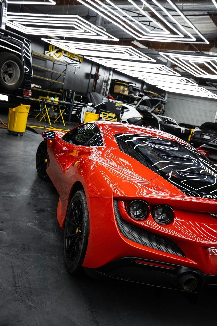 Red sports car in a garage with bright overhead lights.