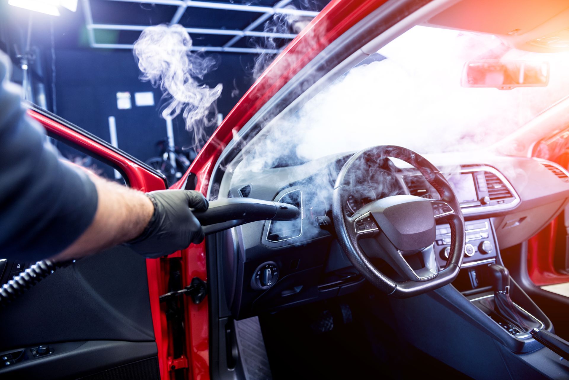 Person steam cleaning the interior of a red car, focusing on the dashboard and steering wheel.