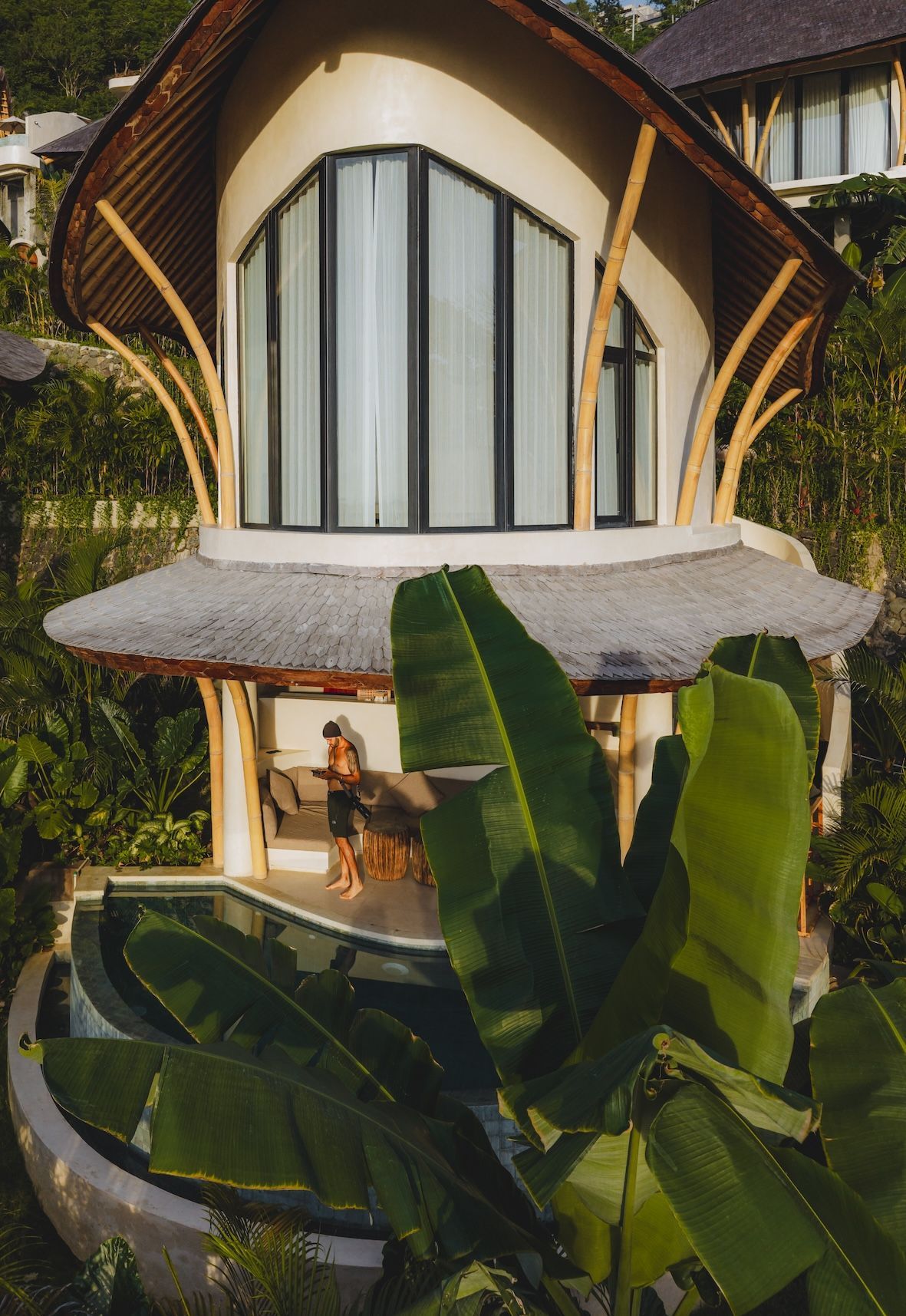 A unique bamboo-style house with a thatched roof, featuring a pool and surrounded by lush greenery.