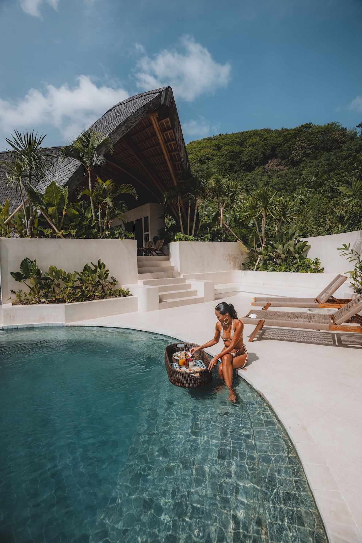 Modern building with a unique, curved roof, pool, and surrounding hillside.