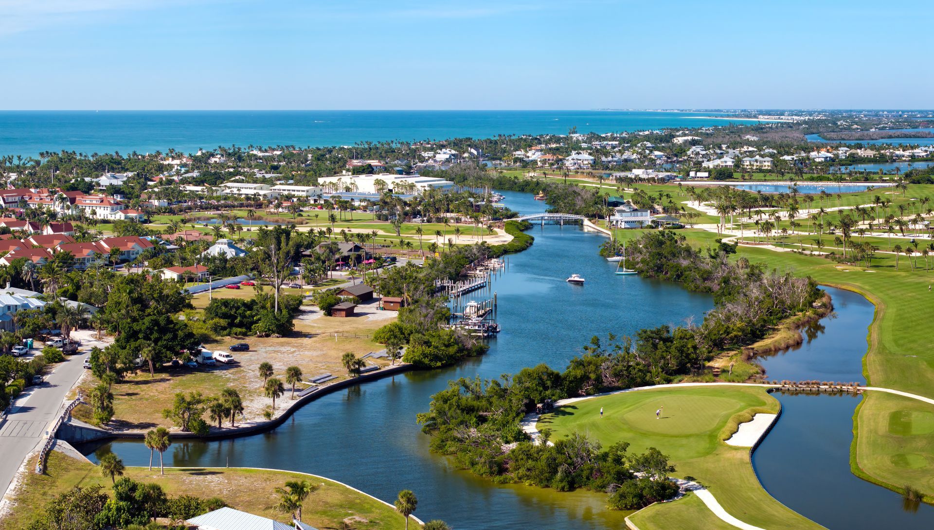 Aerial view of a coastal town with a waterway, golf course, and ocean under a blue sky.