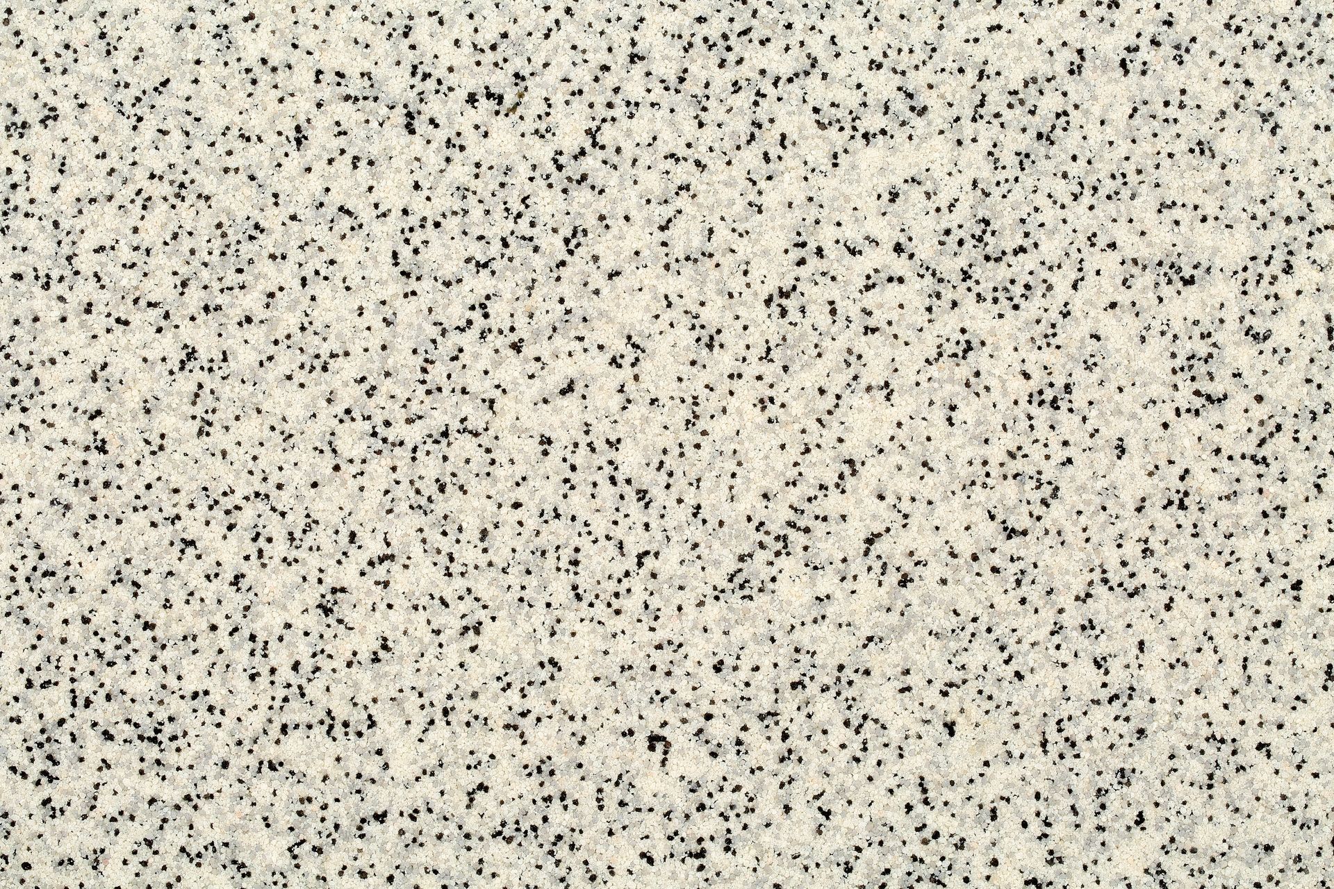 Close-up of a speckled granite surface. Light beige background with many small black dots.