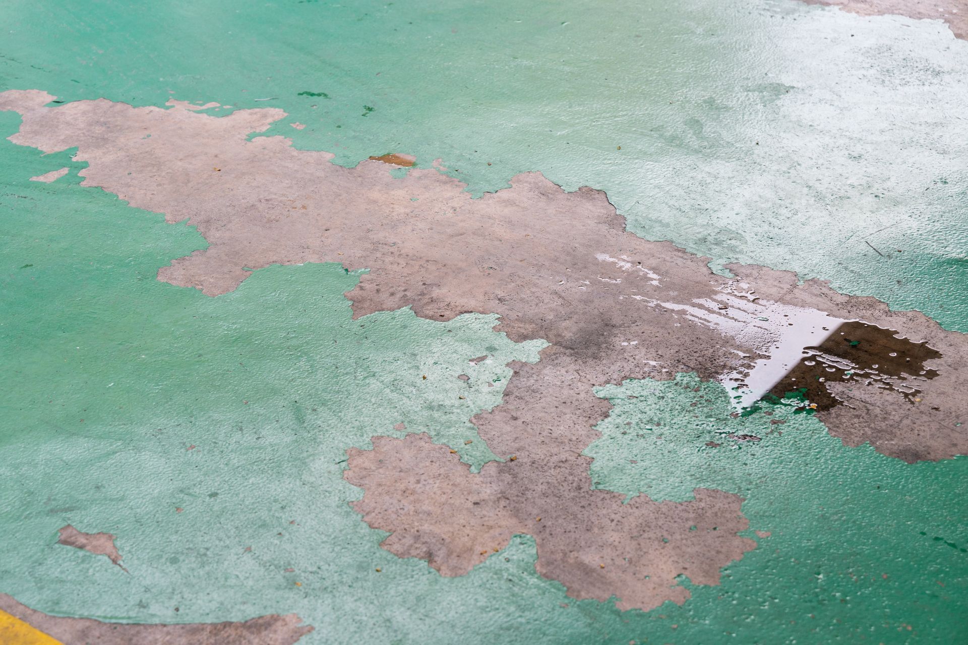 Green and gray paint peeling off concrete surface.