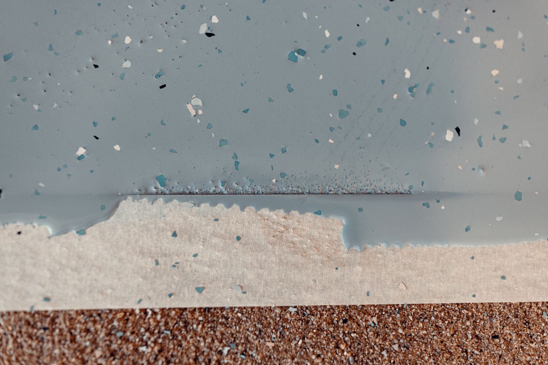 Close-up of a blue speckled surface with a jagged, cut-out edge, revealing a light-colored, textured layer beneath.