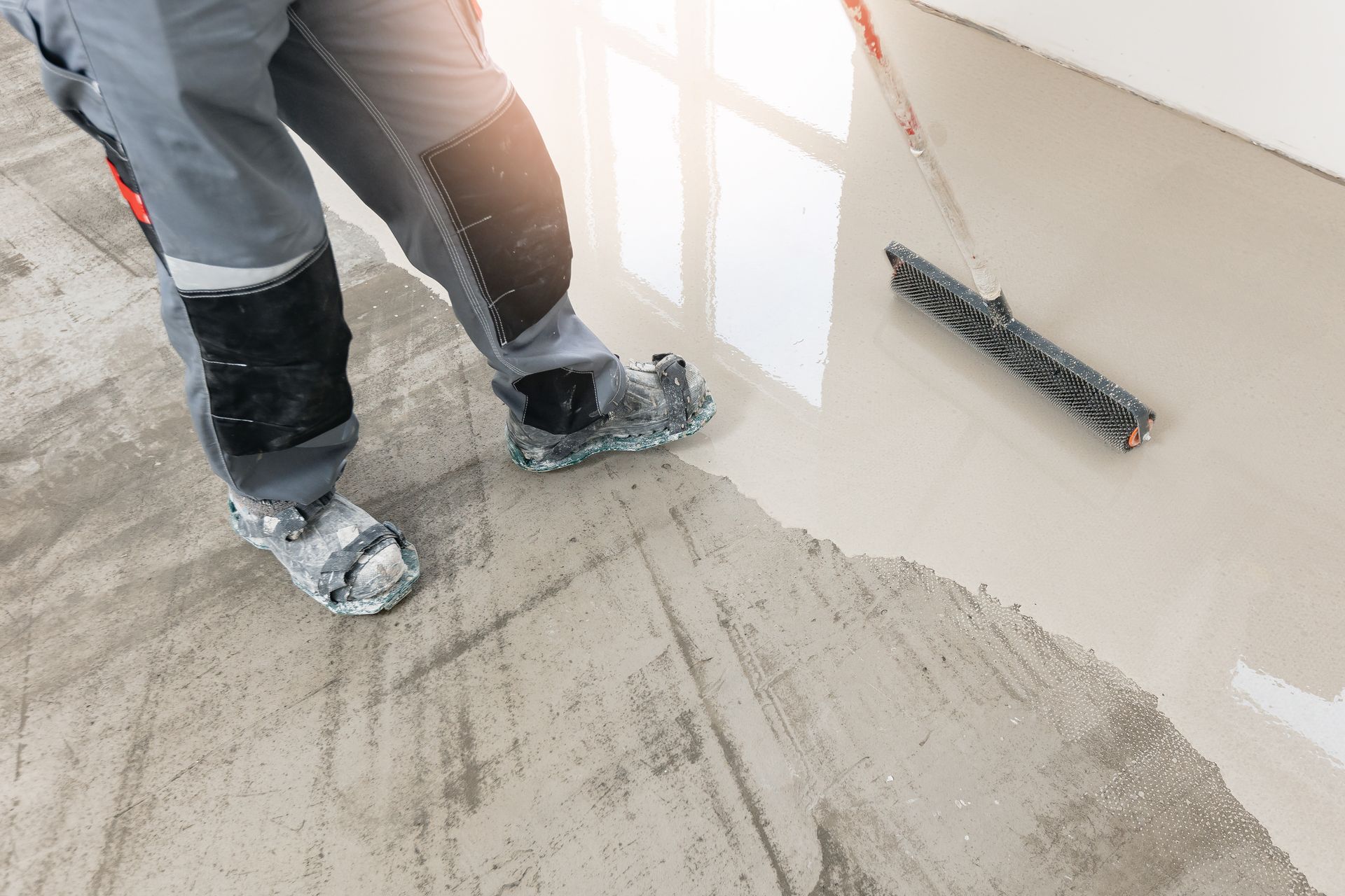 Person smoothing wet concrete floor with a squeegee.