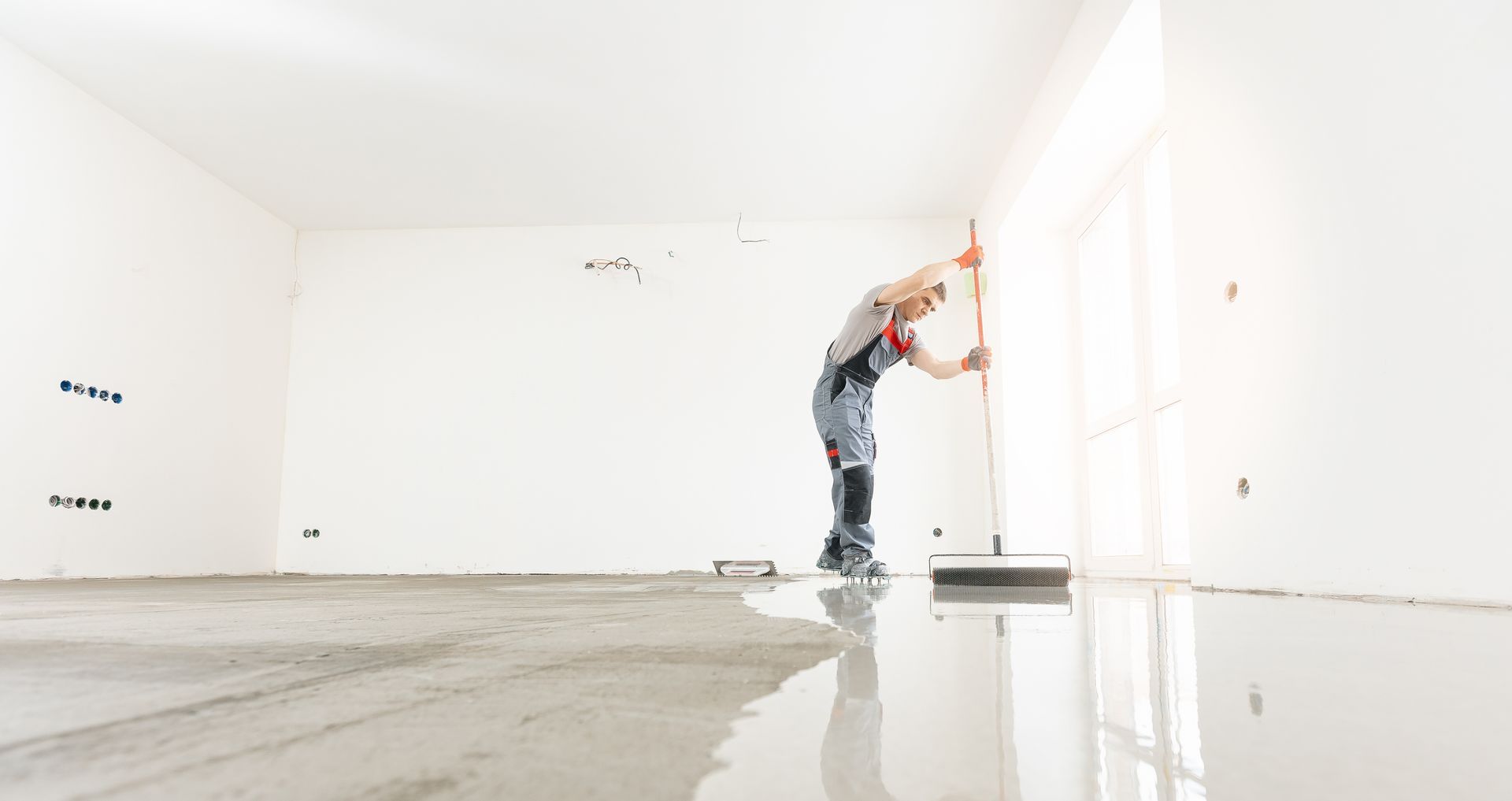 Person smoothing wet floor in an empty white room with a long handled tool.