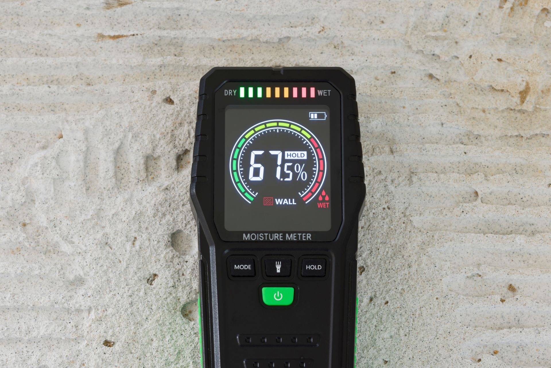 Moisture meter displaying 67%, green and red indicators, on a light-colored surface.