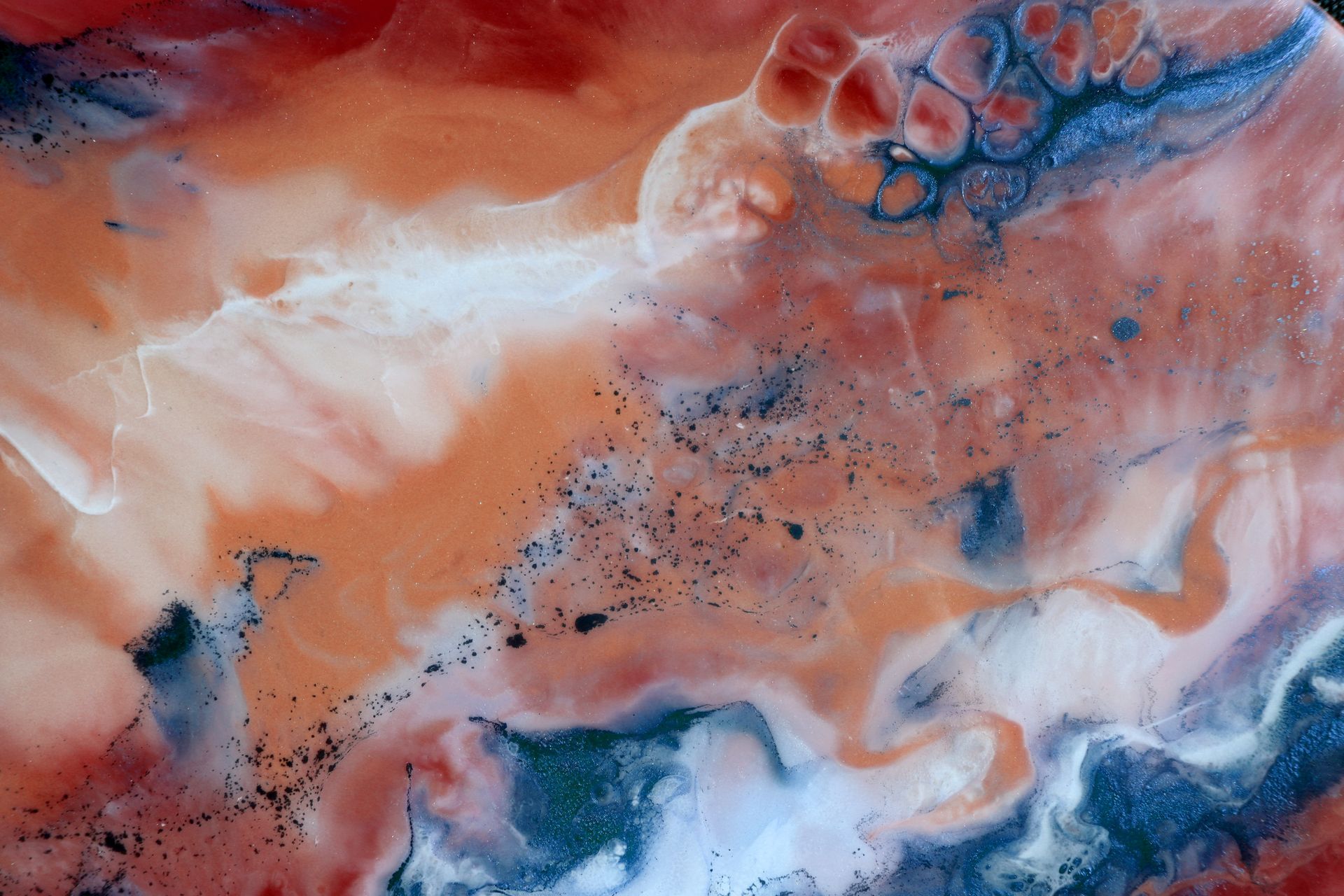 Abstract artwork with swirling orange, blue, and white hues. Dark speckles and bubbly textures add depth.