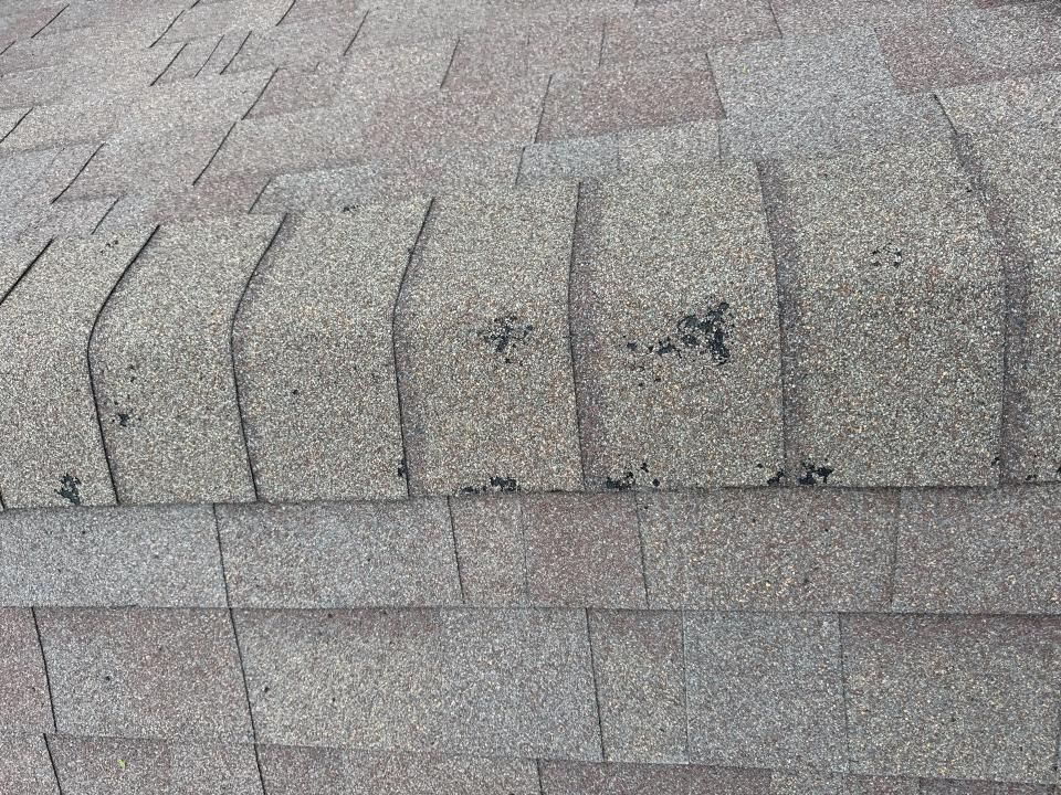 Close-up view of a brown asphalt shingle roof. Some shingles show dark spots, suggesting age or damage.