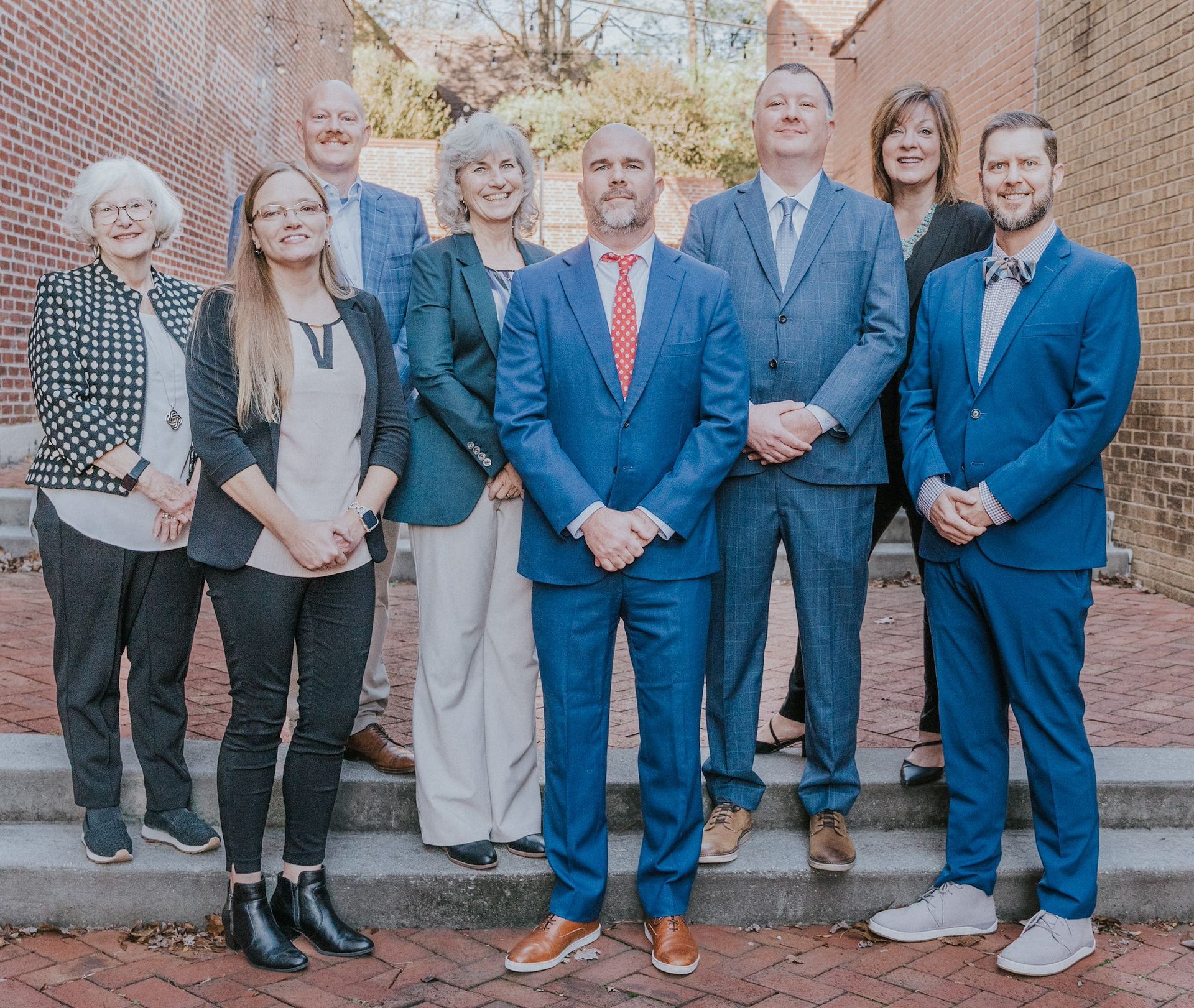 Group of people in business attire standing on steps outdoors in front of a brick building.