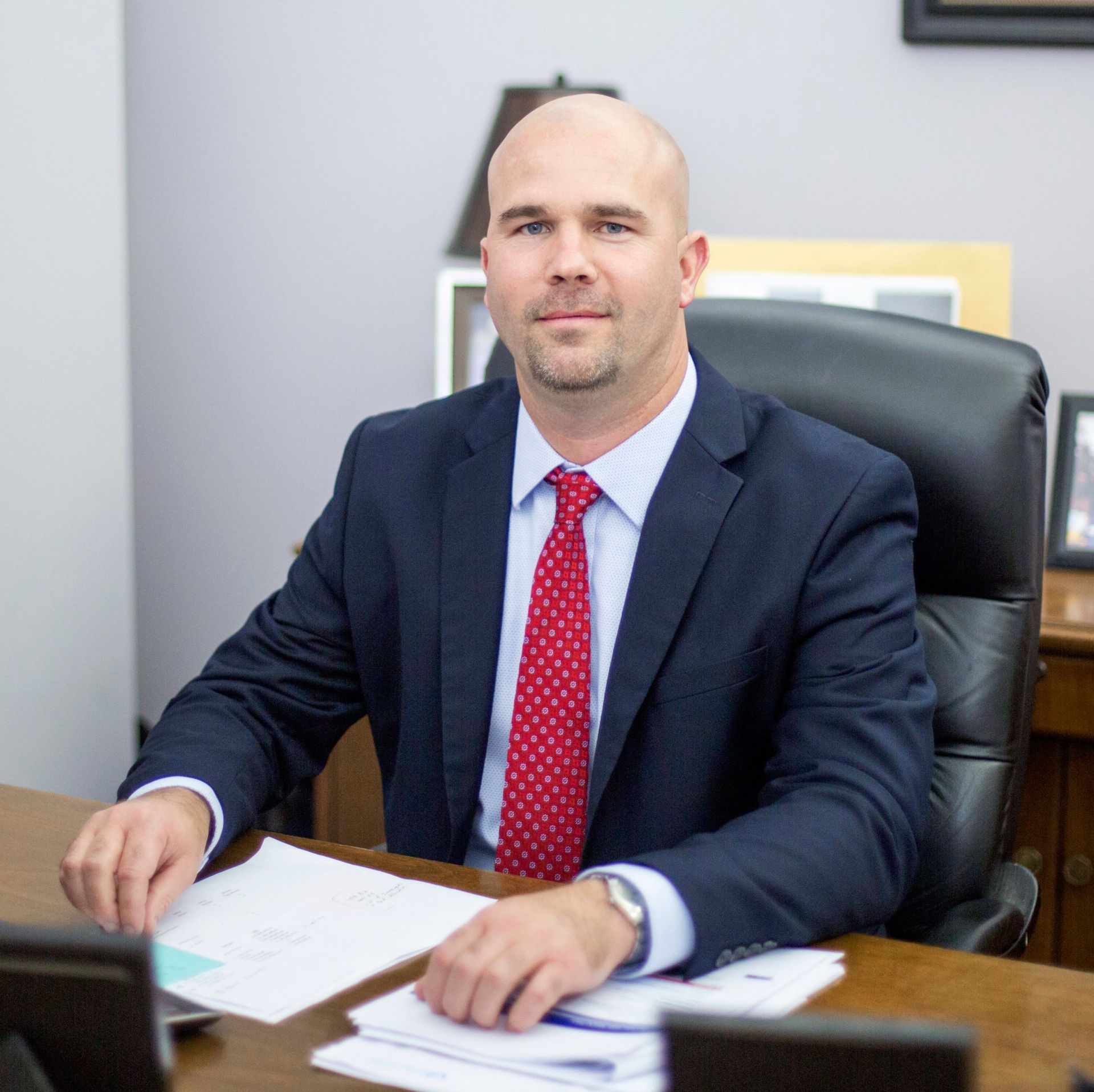 Man in a suit, seated at a desk, looking at the camera.