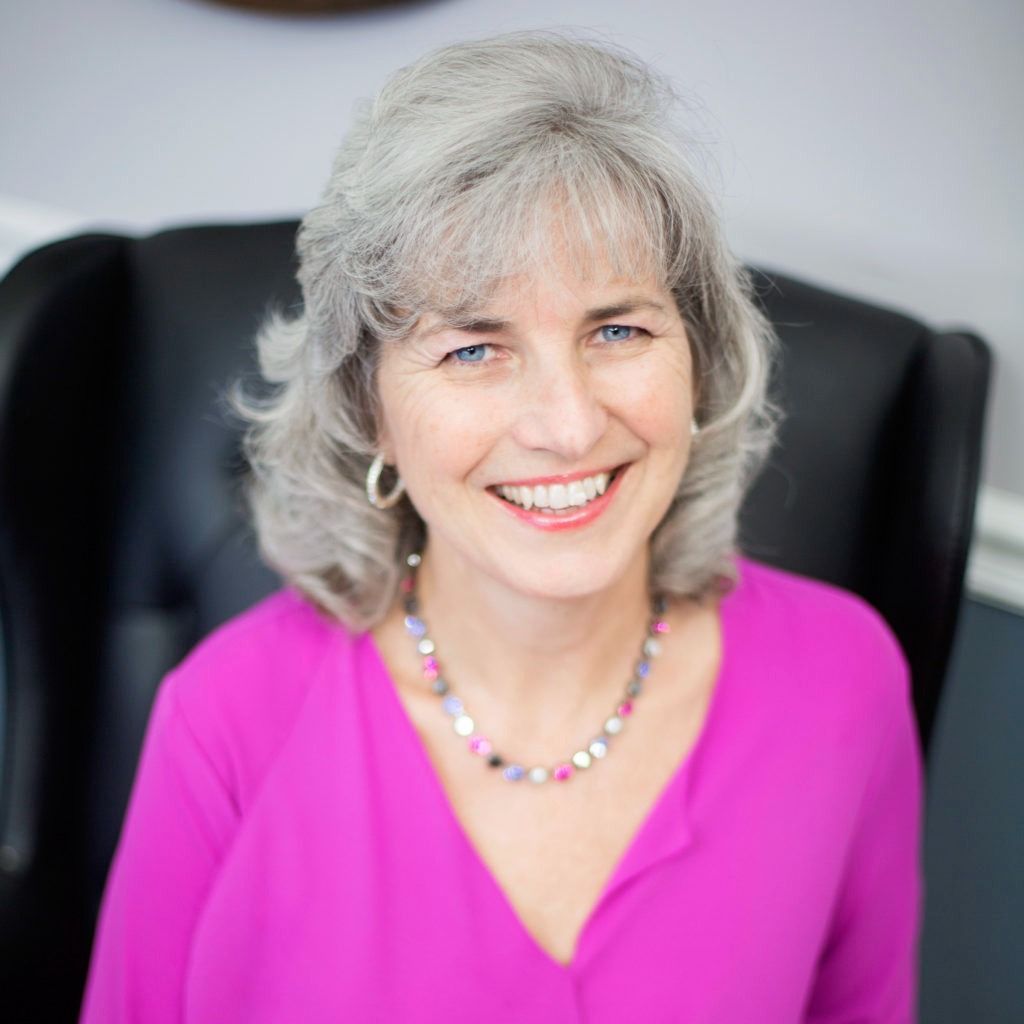 Man in a suit, seated at a desk, looking at the camera.