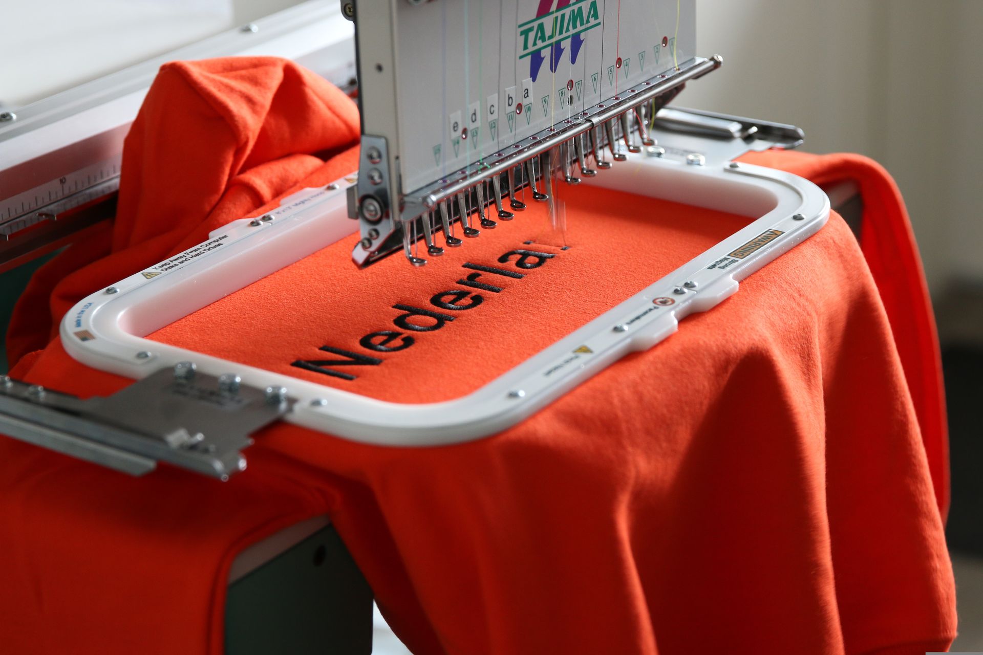 An orange shirt is being embroidered with the word nederland on it