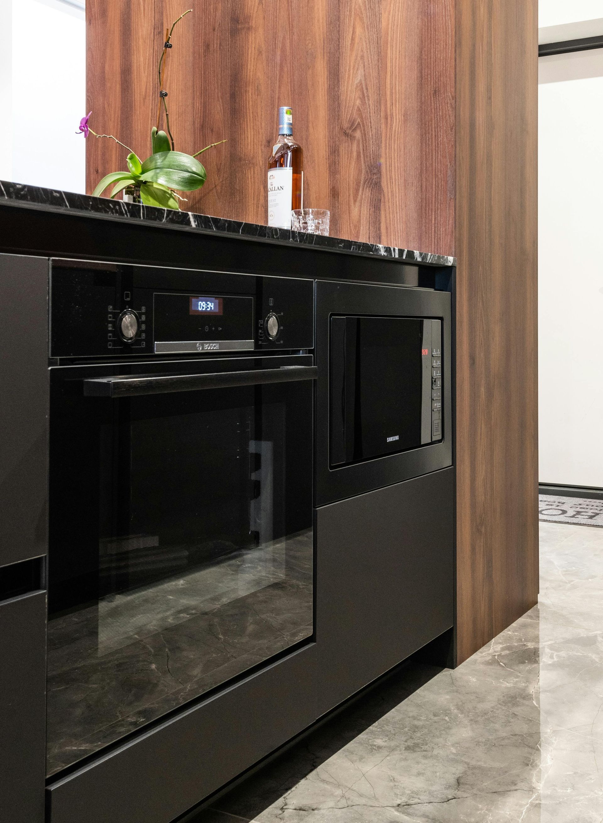 Built-in black oven and microwave in a modern kitchen with dark wood paneling and a black countertop.