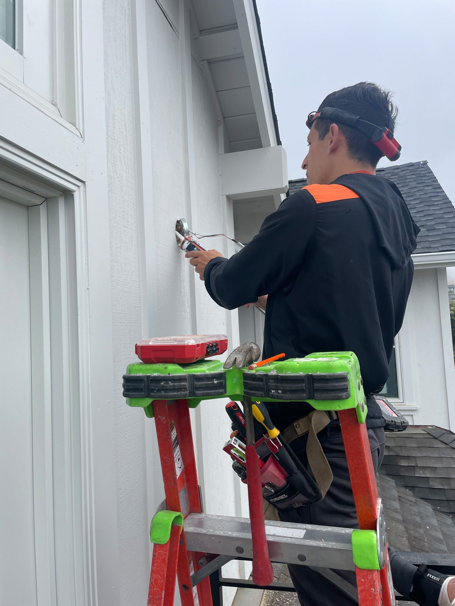 A man is standing on a ladder painting a white house.