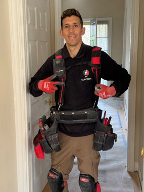 A man wearing a tool belt and gloves is standing in a hallway.