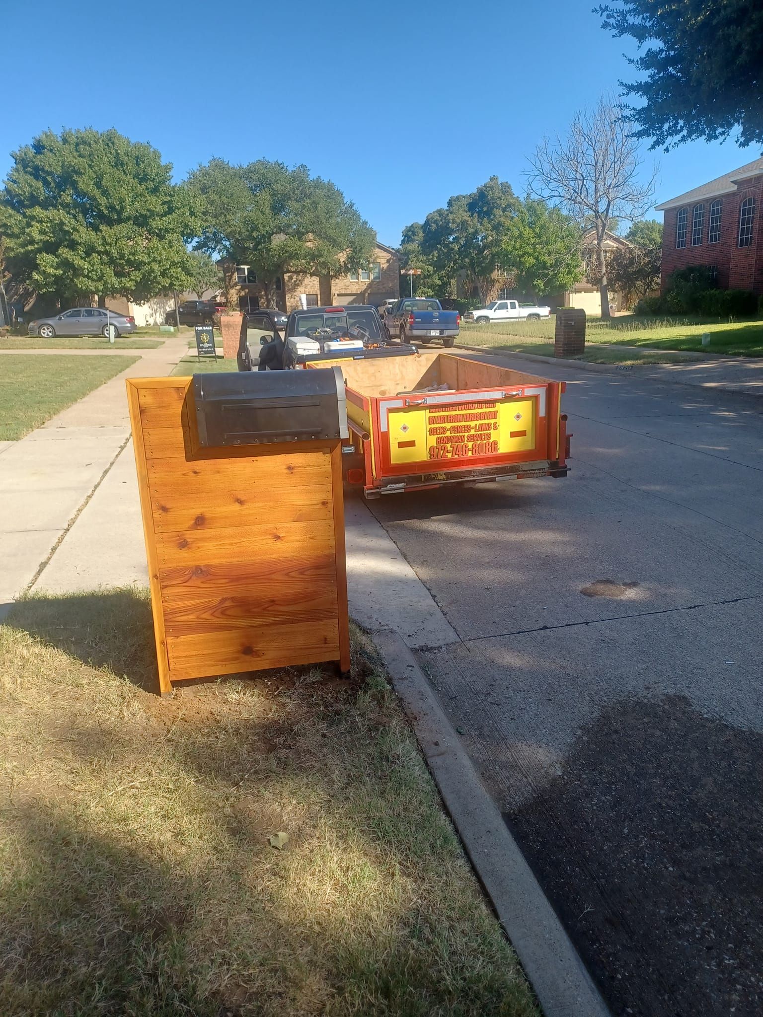 A wooden trash can is sitting on the side of the road next to a trailer.