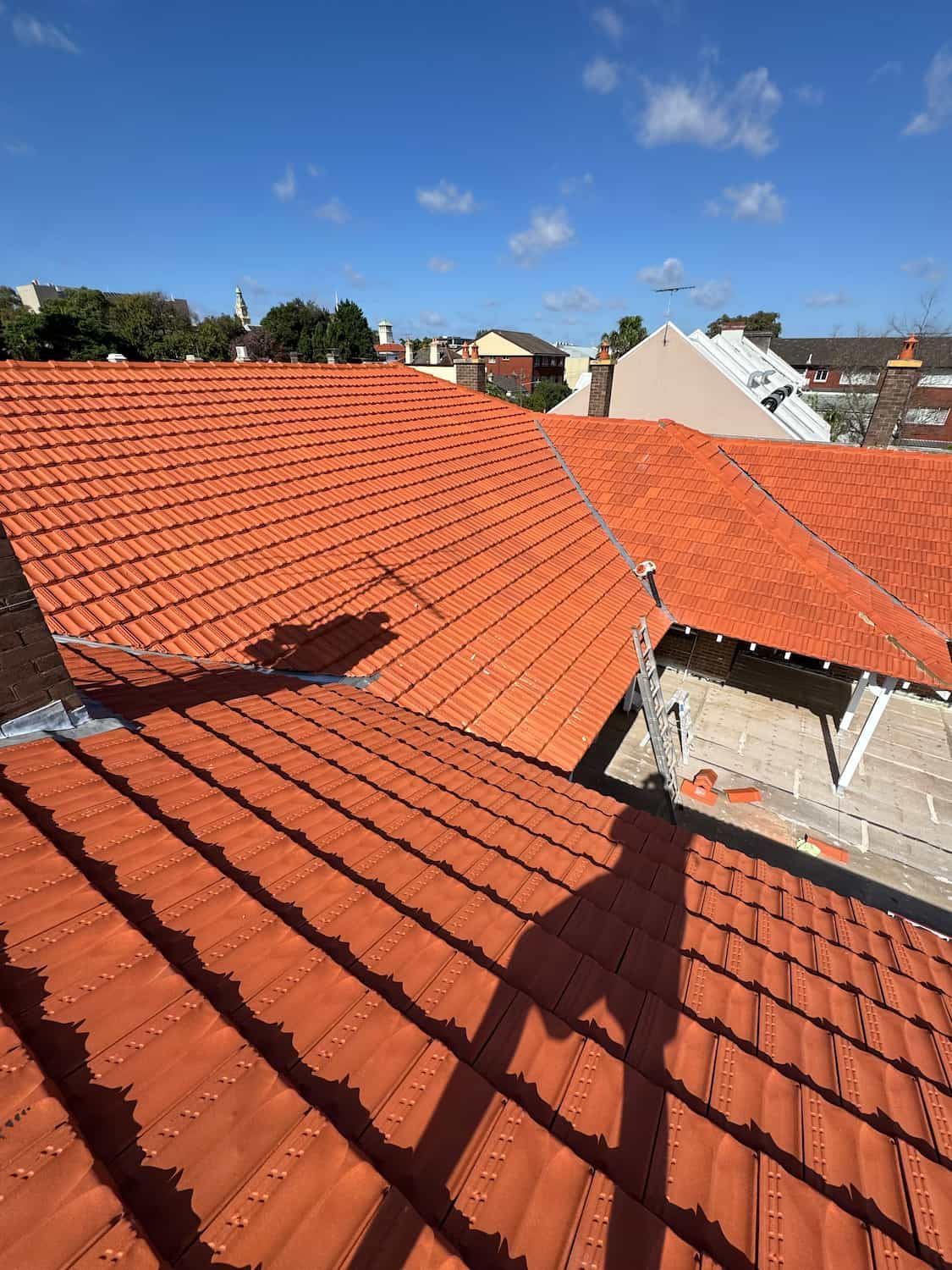 A Red Tiled Roof With a Blue Sky in the Background — DC Roofing In Leichhardt, NSW