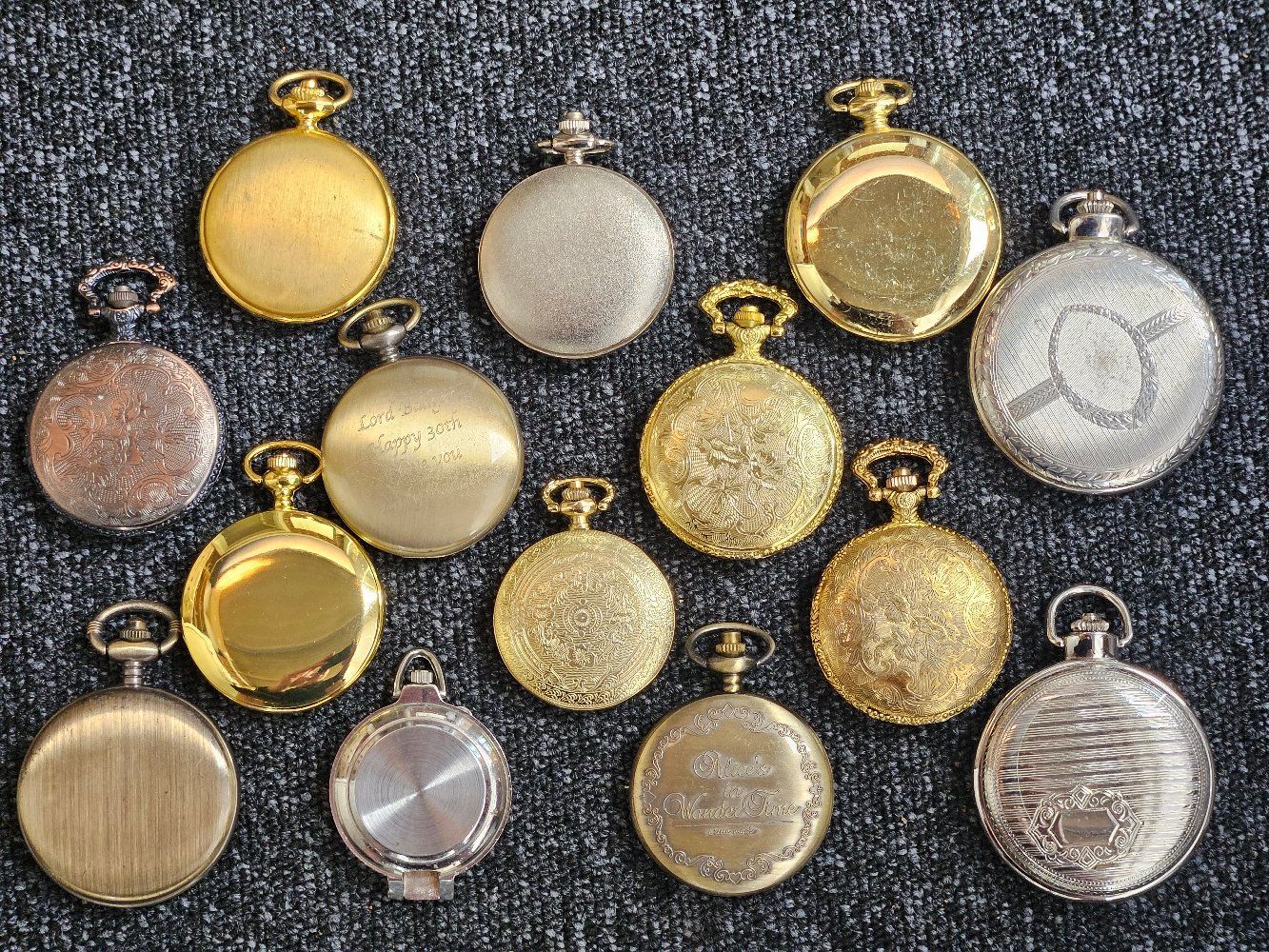 Assortment of gold and silver pocket watches arranged on a textured, dark gray surface.