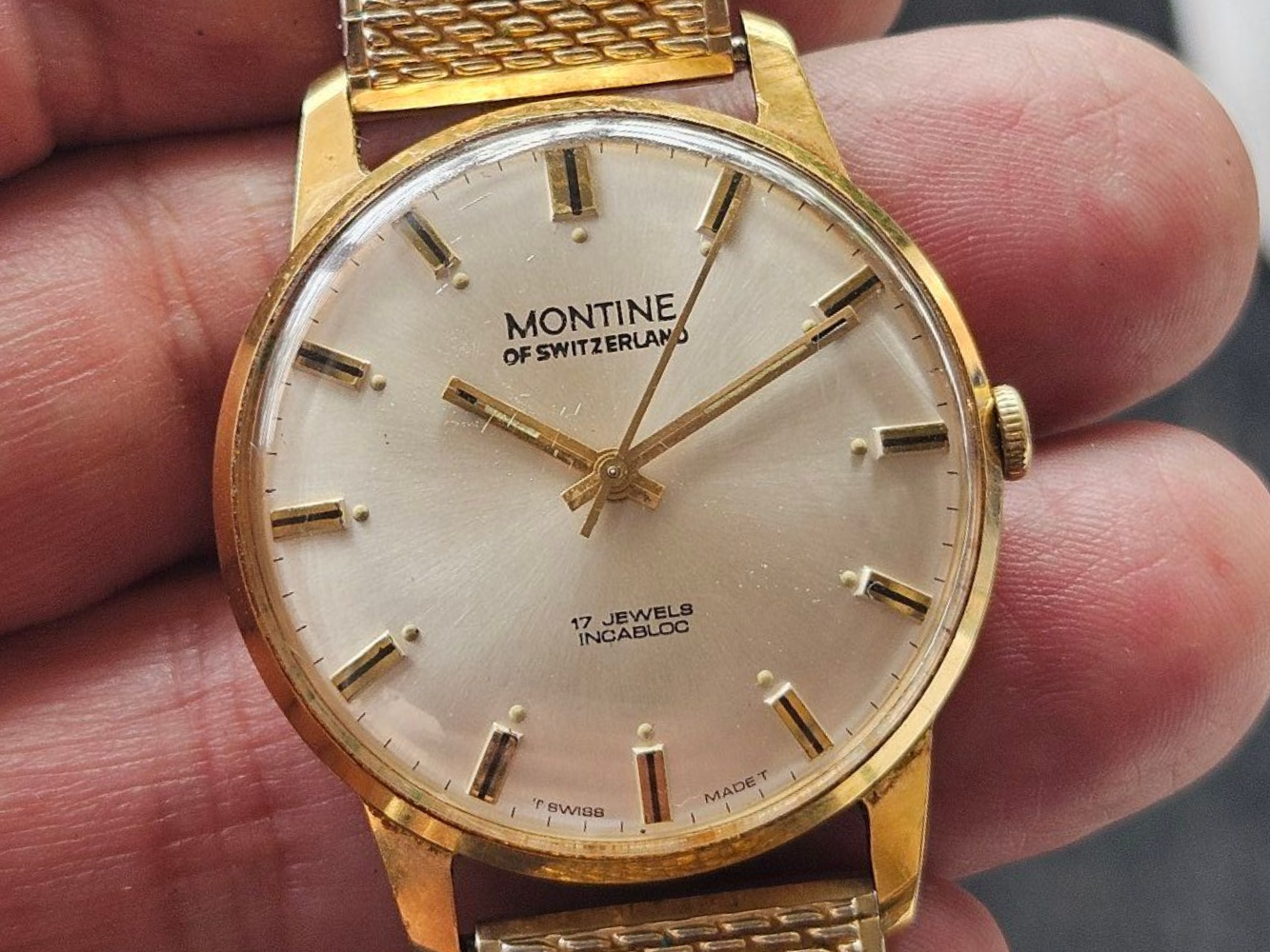 Gold Montine Swiss wristwatch with gold hands and hour markers on a light-colored face.