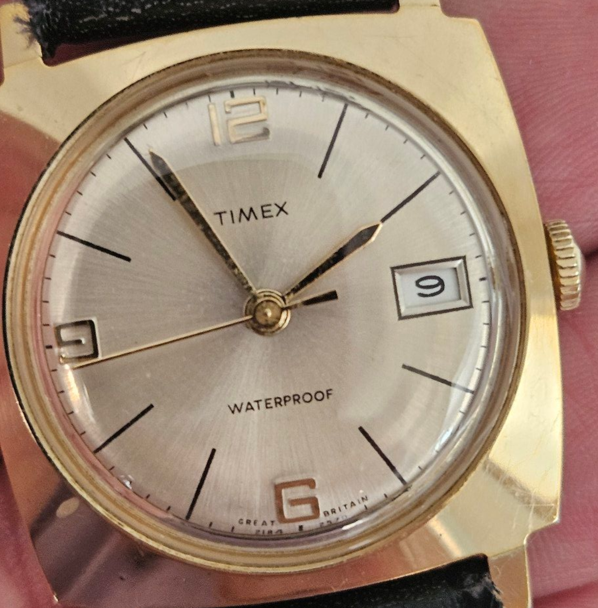 Gold Timex wristwatch with a light-colored face, date window, and black strap.