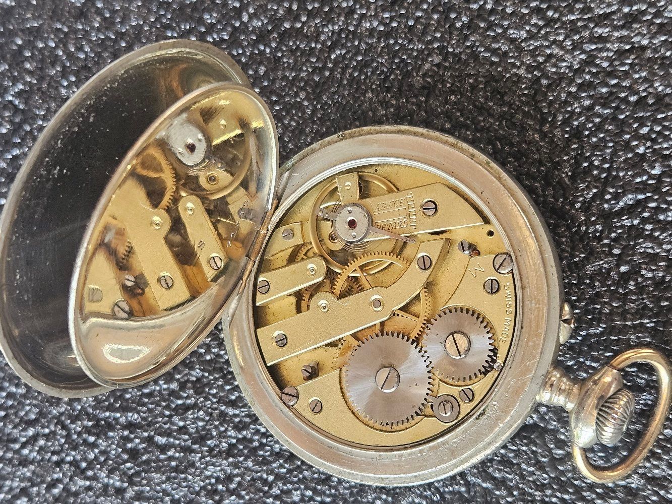 Open pocket watch, showing intricate gold-colored gears and mechanisms within a silver case.