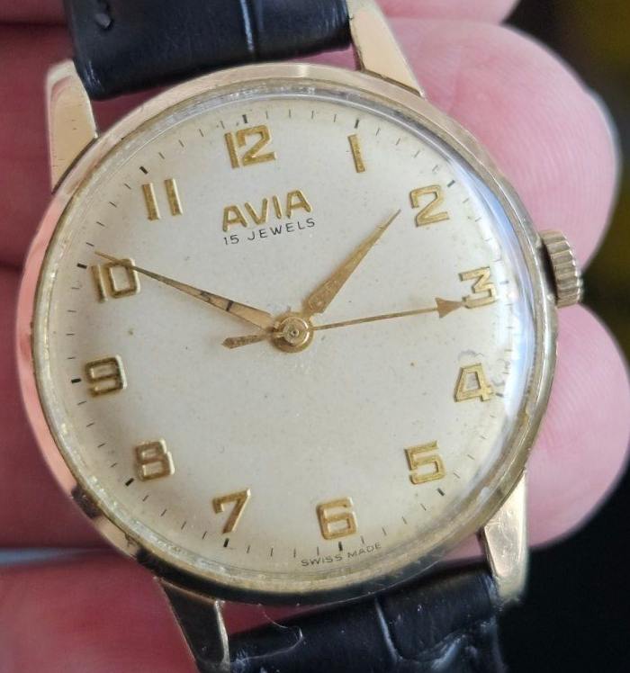 Gold-toned Avia wristwatch with a cream dial, black strap, and gold numerals and hands.