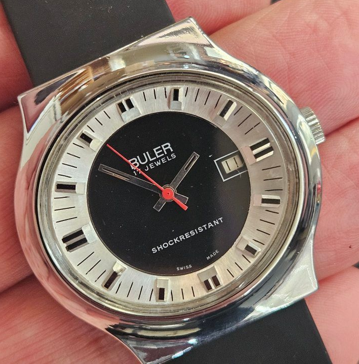 A silver Buler watch with a black face, white markers, and red hands, on a black band.