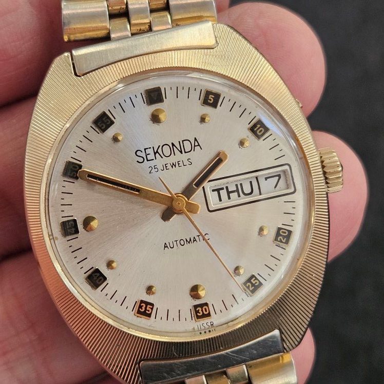 Gold Sekonda wristwatch with a white face, day/date display, and gold hands/markers.