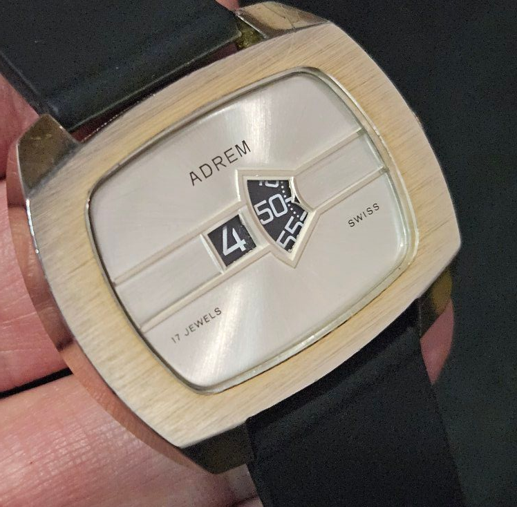 Gold-toned ADREM watch with a white face, black digital time display, and black band. Swiss made.
