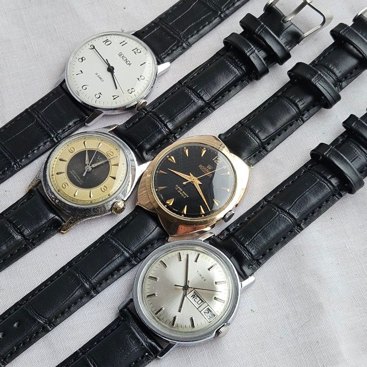 Four vintage wristwatches with black leather straps, displayed on a surface.