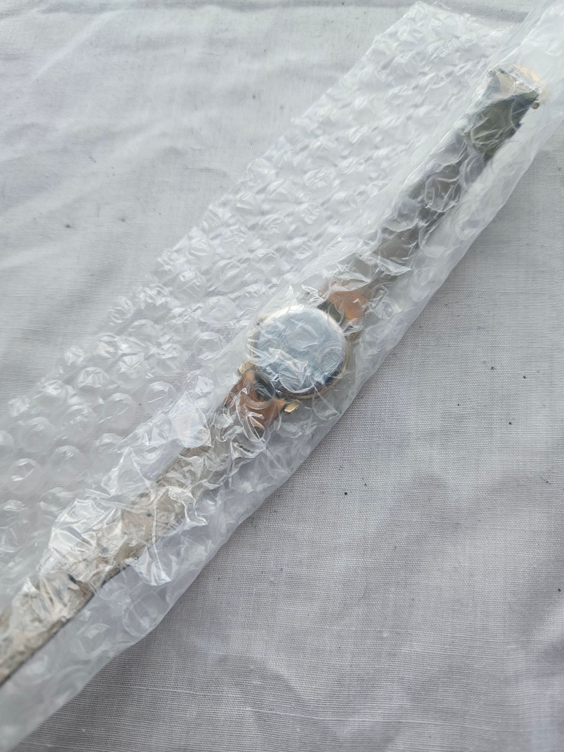 Watch with silver band, wrapped in bubble wrap on white fabric.