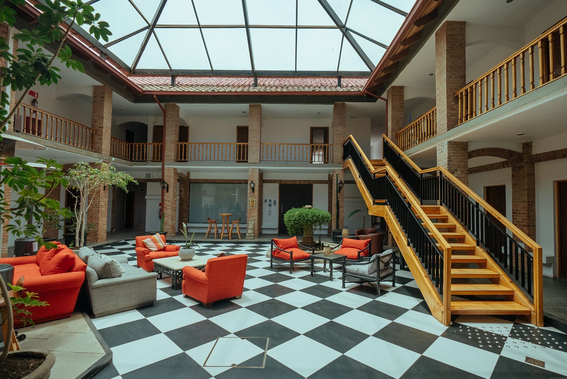 Atrium lounge with red chairs, black-and-white checkered floor, skylight ceiling, and wooden stairs