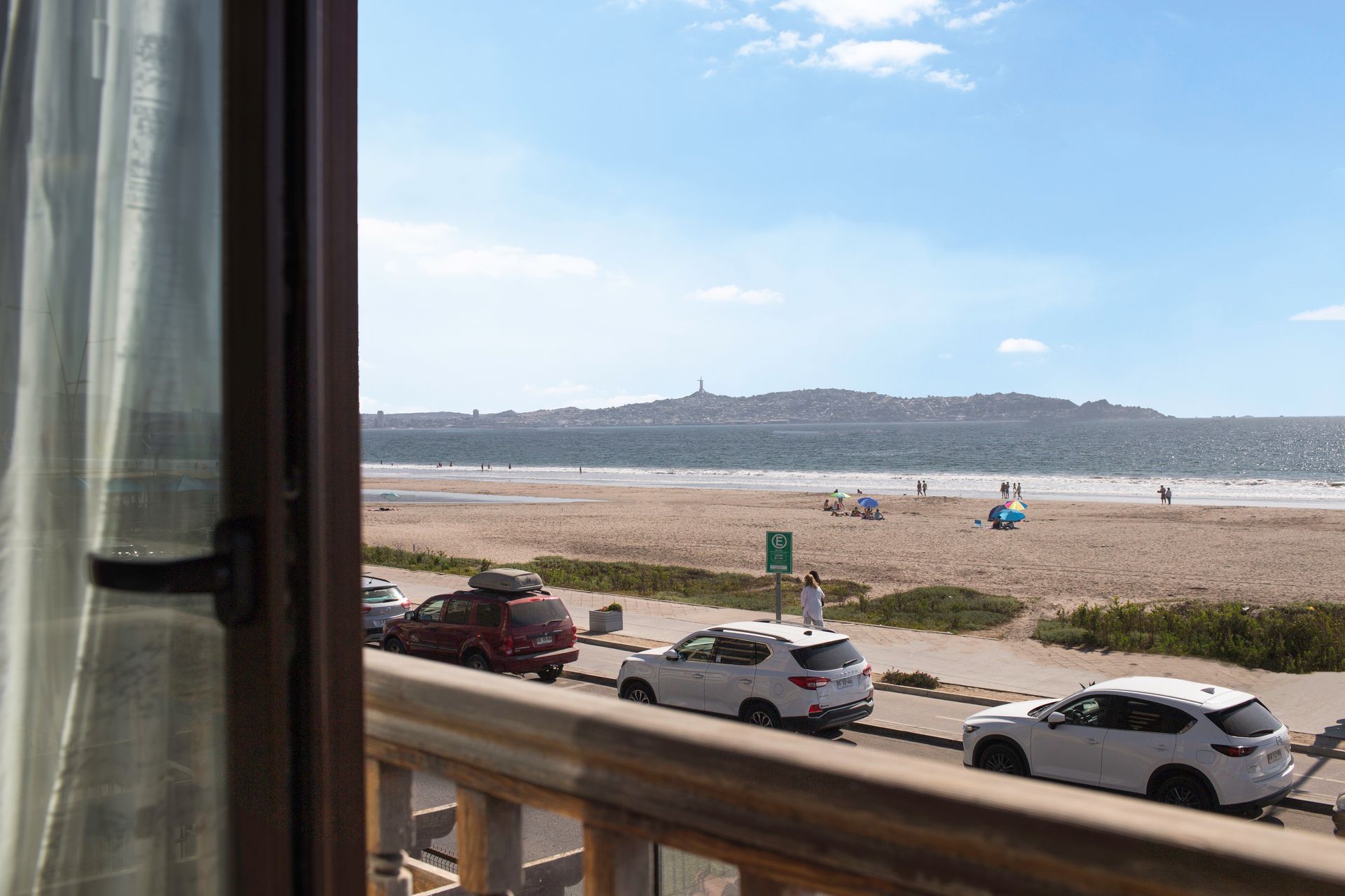 A view of a beach from a balcony with cars parked on the side of the road.