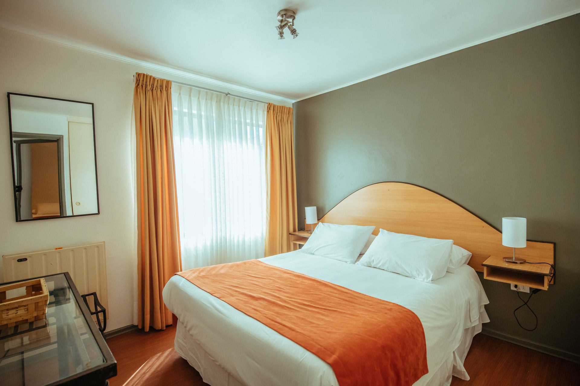 A hotel room with a bed , mirror , nightstand , and window.