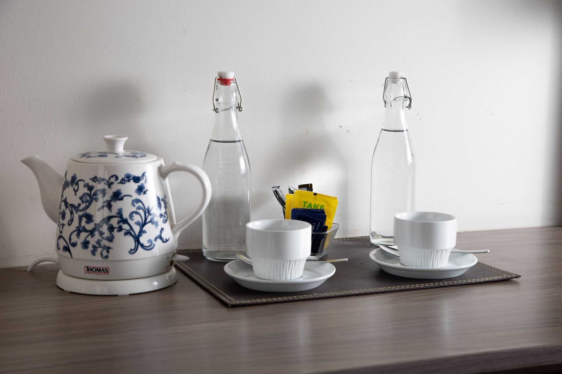 A teapot , cups , saucers , and bottles of water are on a table.