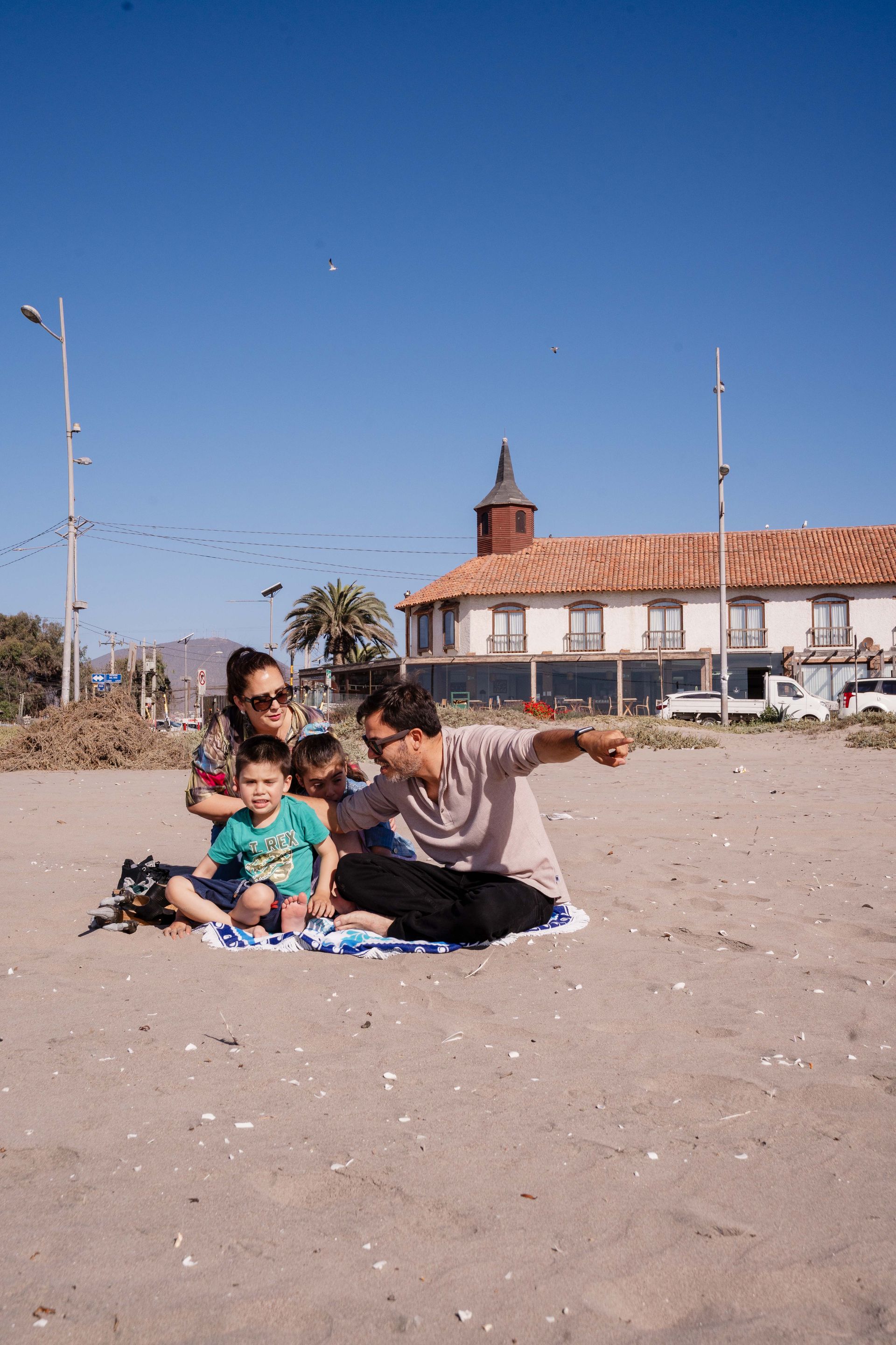 Couple walking on a sandy beach in front of a seaside house under a clear blue sky
