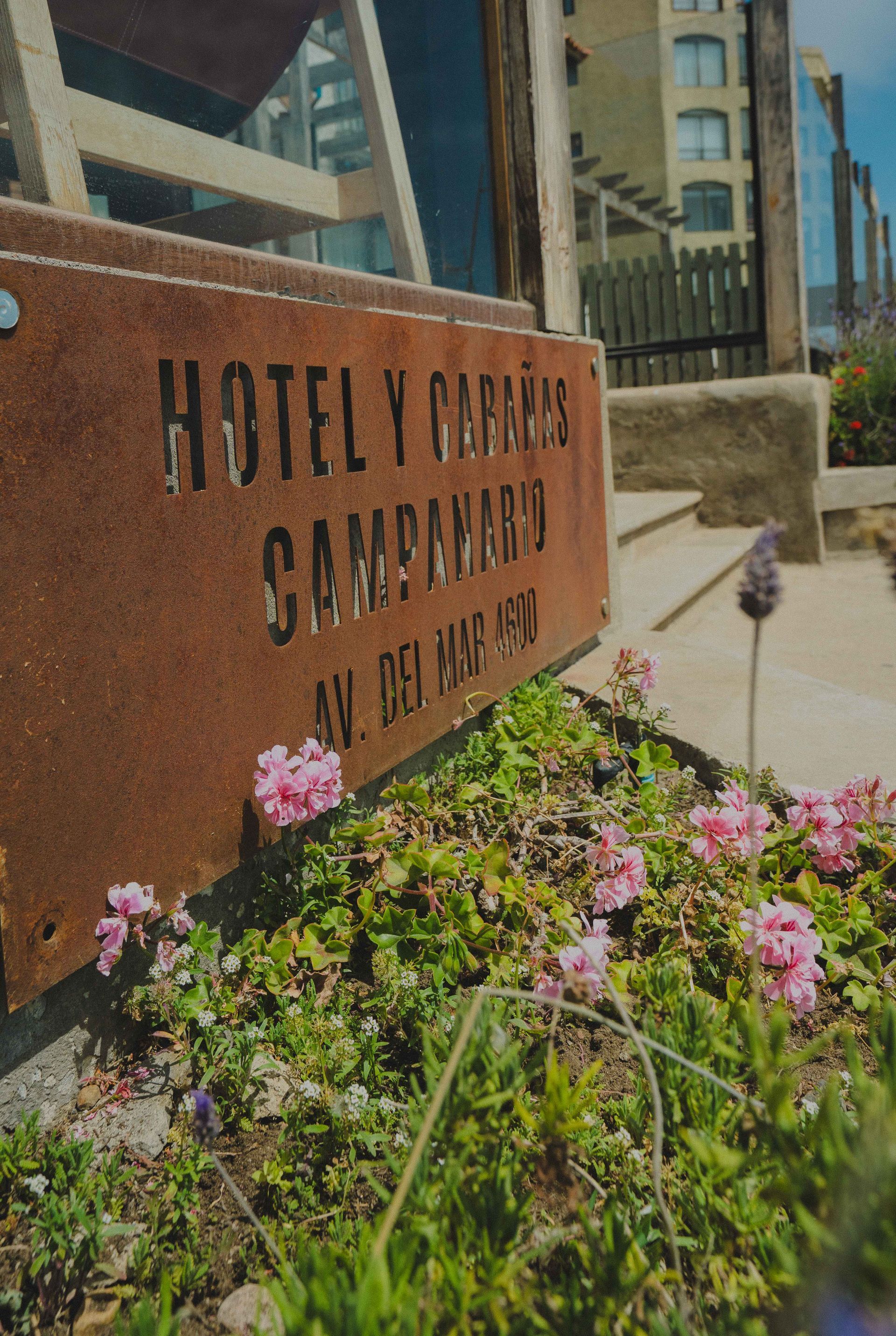Hotel V Maryland sign beside pink flowers and a walkway by modern buildings