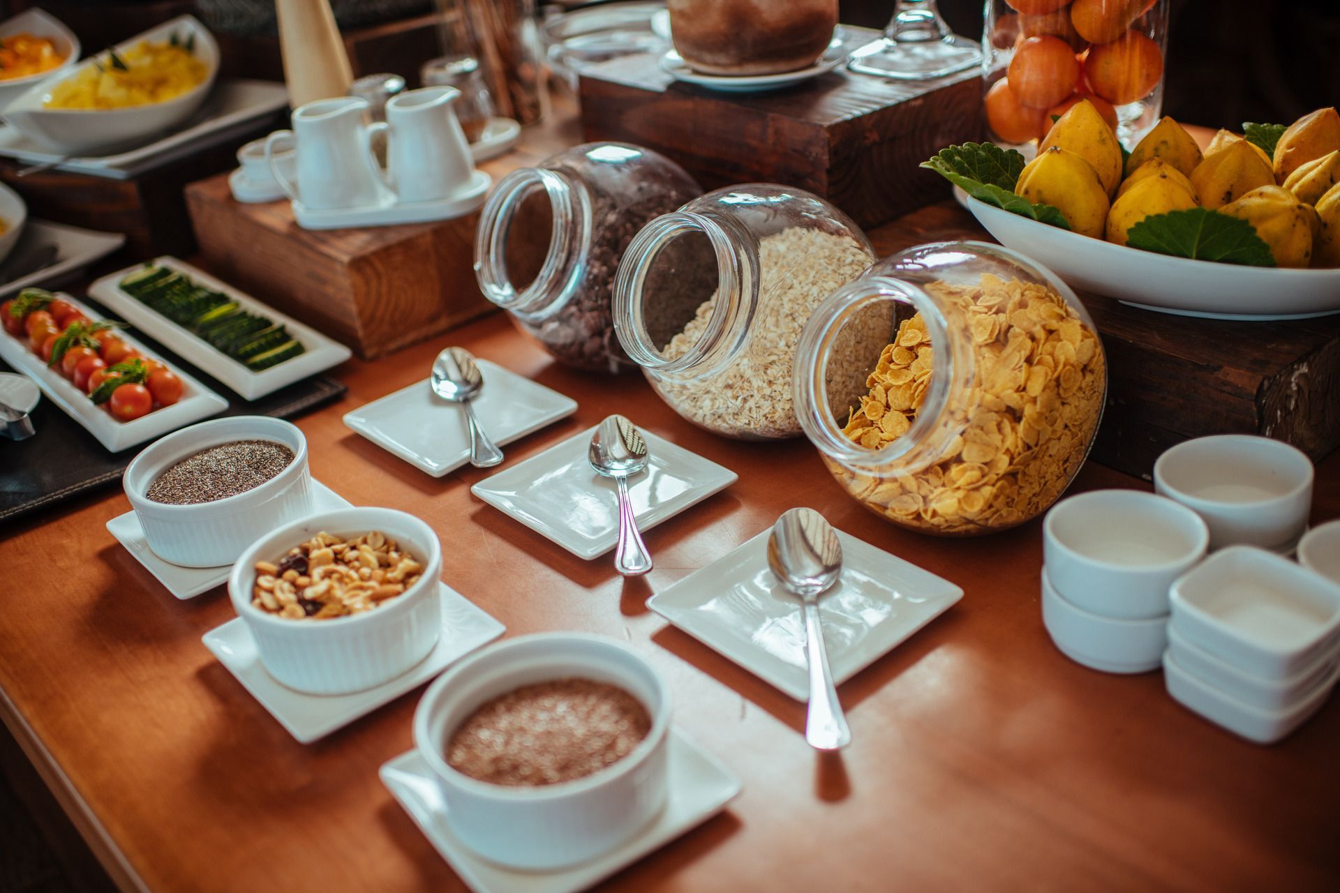 Breakfast buffet with cereals, pastries, fruit, yogurt, and white dishes on a wooden table.