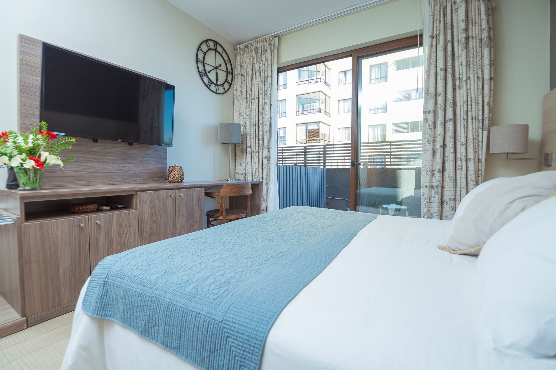A hotel room with a bed , television , desk and balcony.